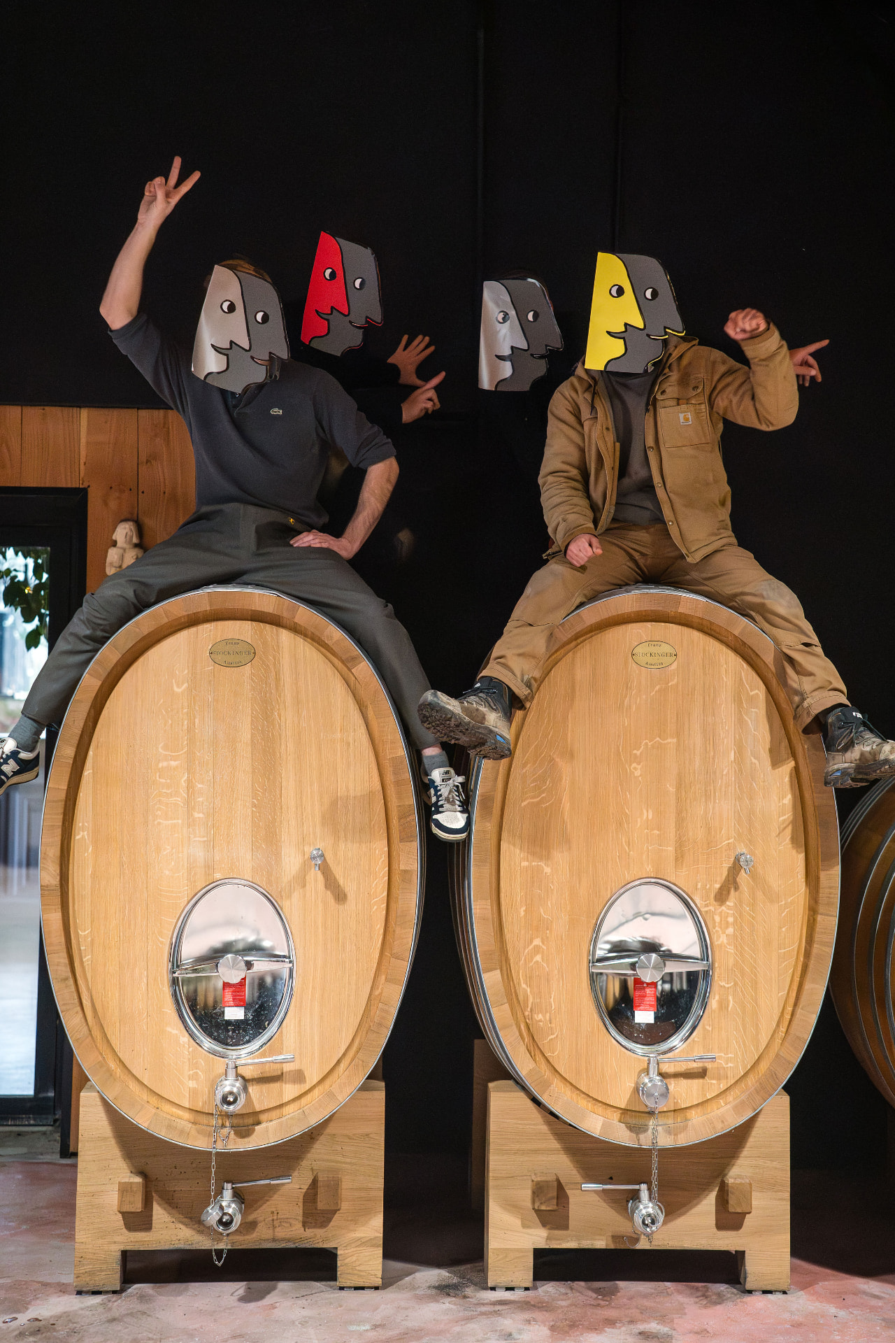 Deux vignerons du Domaine F. Mabileau assis sur des fûts de chêne, masques colorés sur le visage