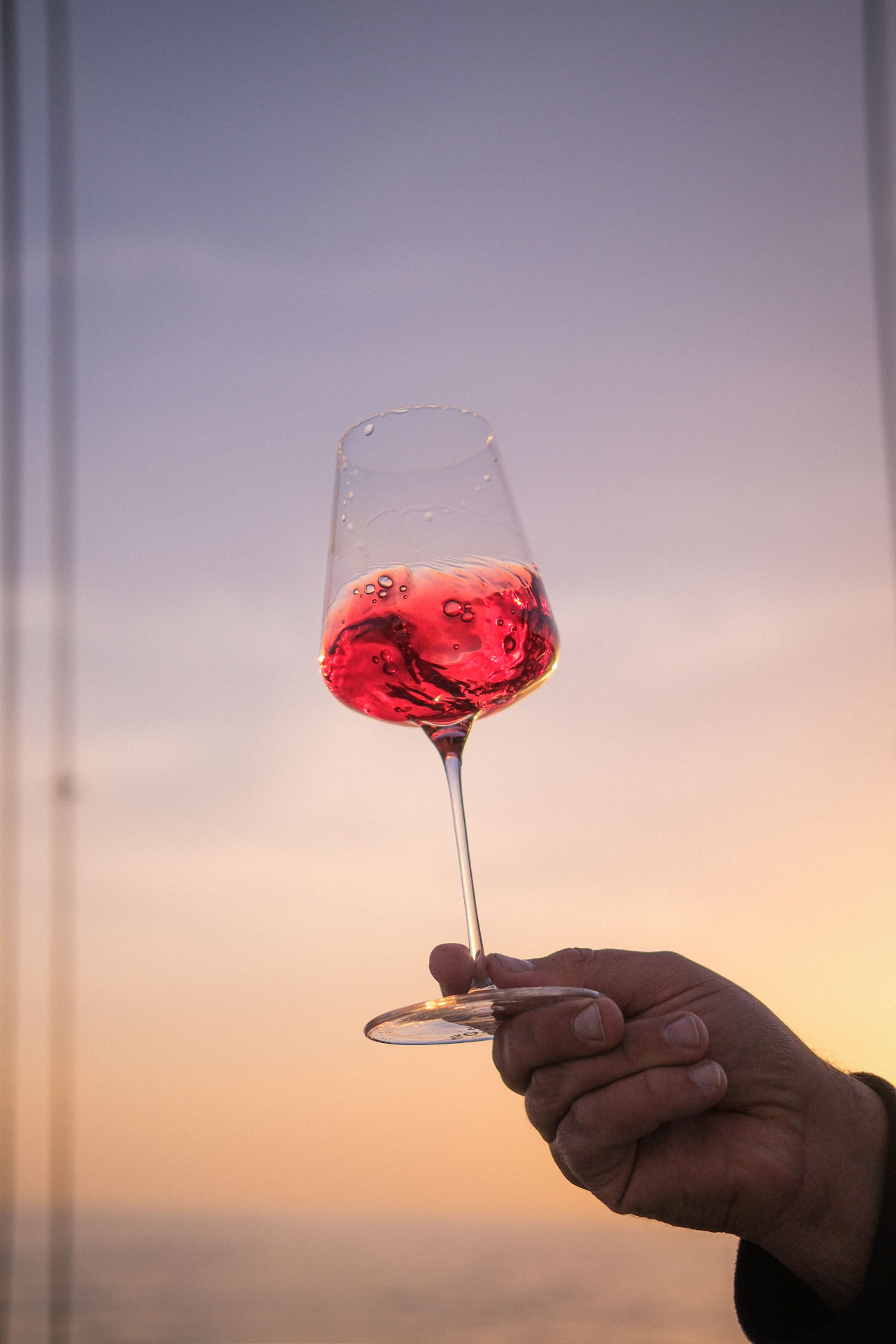 Verre de vin rosé tenu à la main face au coucher de soleil sur l'océan, oenotourisme en Loire-Atlantique